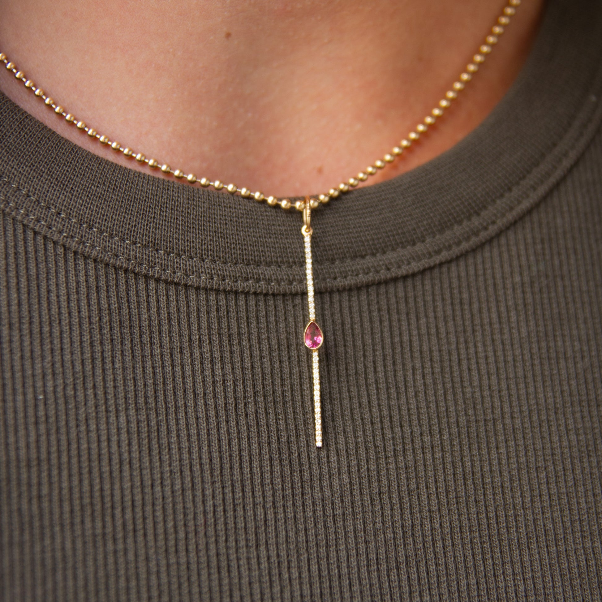 Necklace with a pink gemstone on a person wearing a brown ribbed shirt