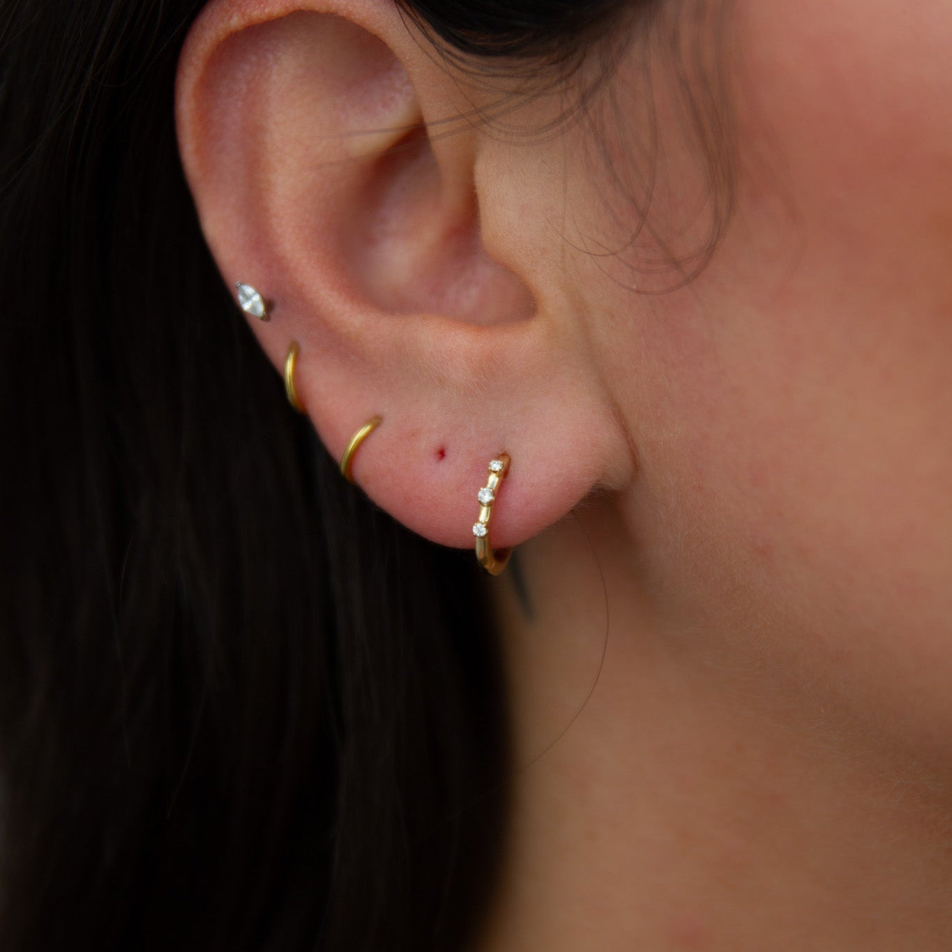 Close-up of an ear with gold hoop earrings and a small stud.