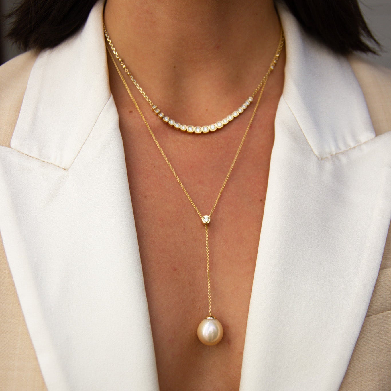 Close-up of a person wearing a gold necklace with a pearl pendant against a neutral background.