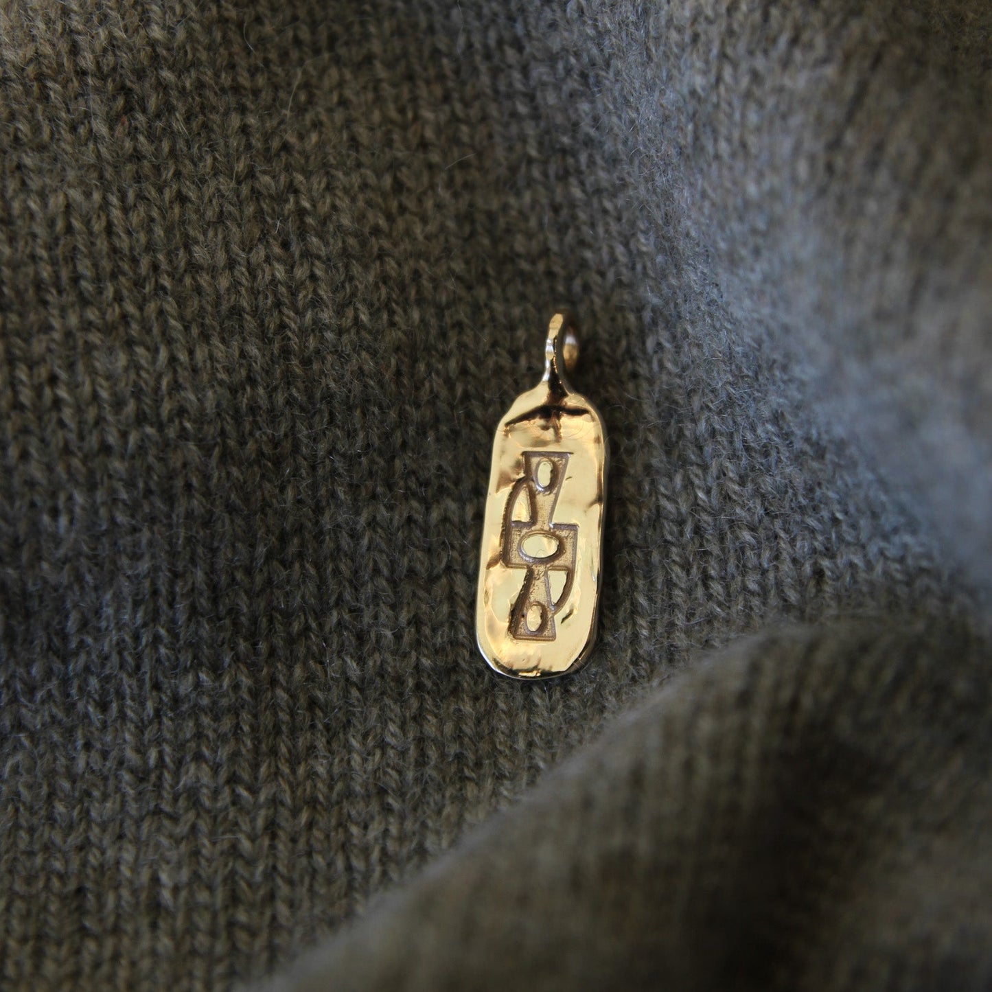 Gold pendant with hieroglyphics on a textured dark fabric background