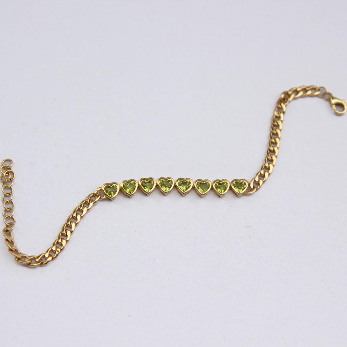 Gold bracelet with heart-shaped green gemstones on a white background