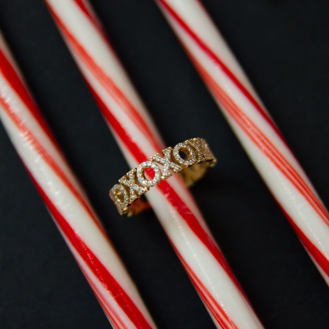 Gold ring with 'XOXO' design on red and white striped candy canes against a dark background