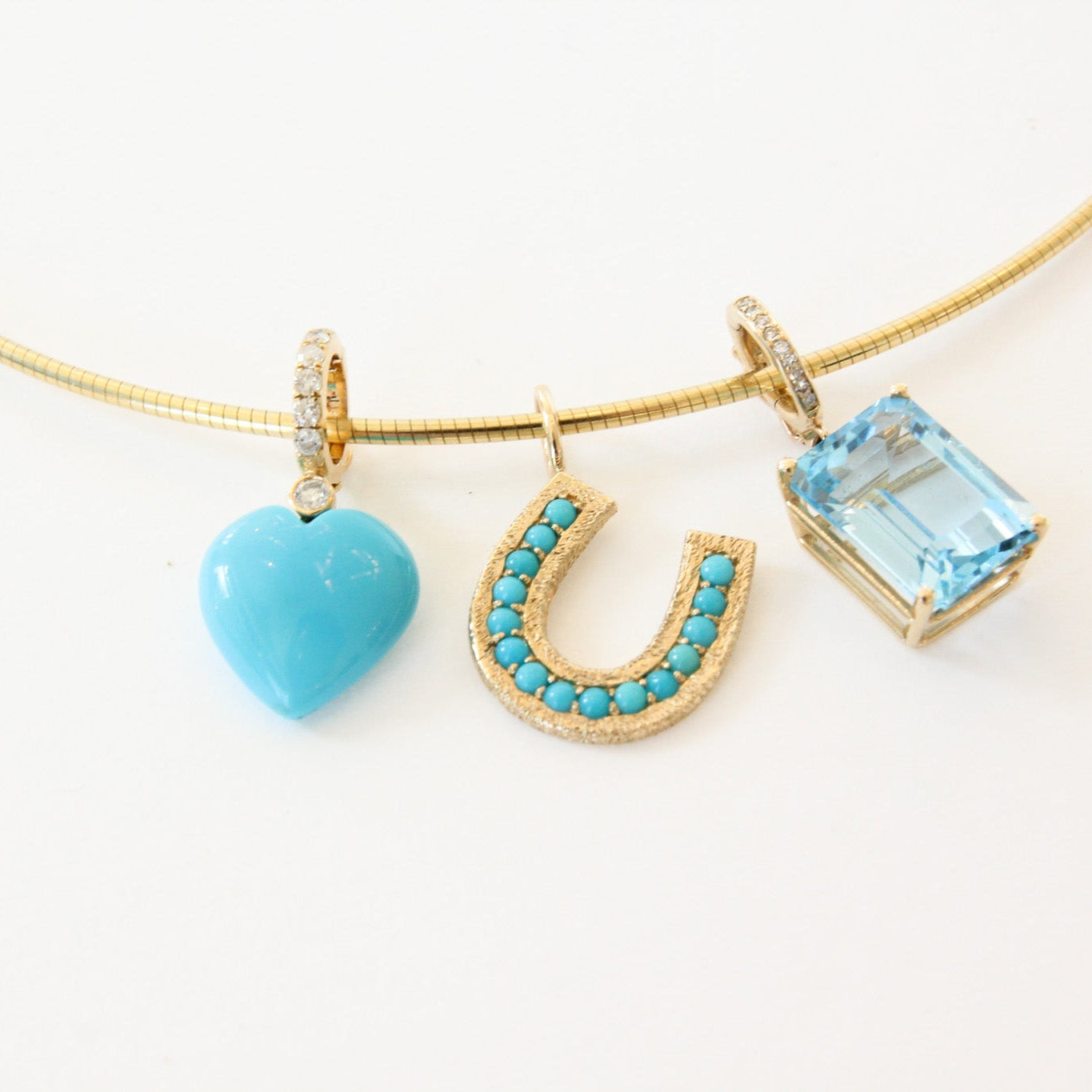 Three turquoise gemstone pendants on a gold chain against a white background