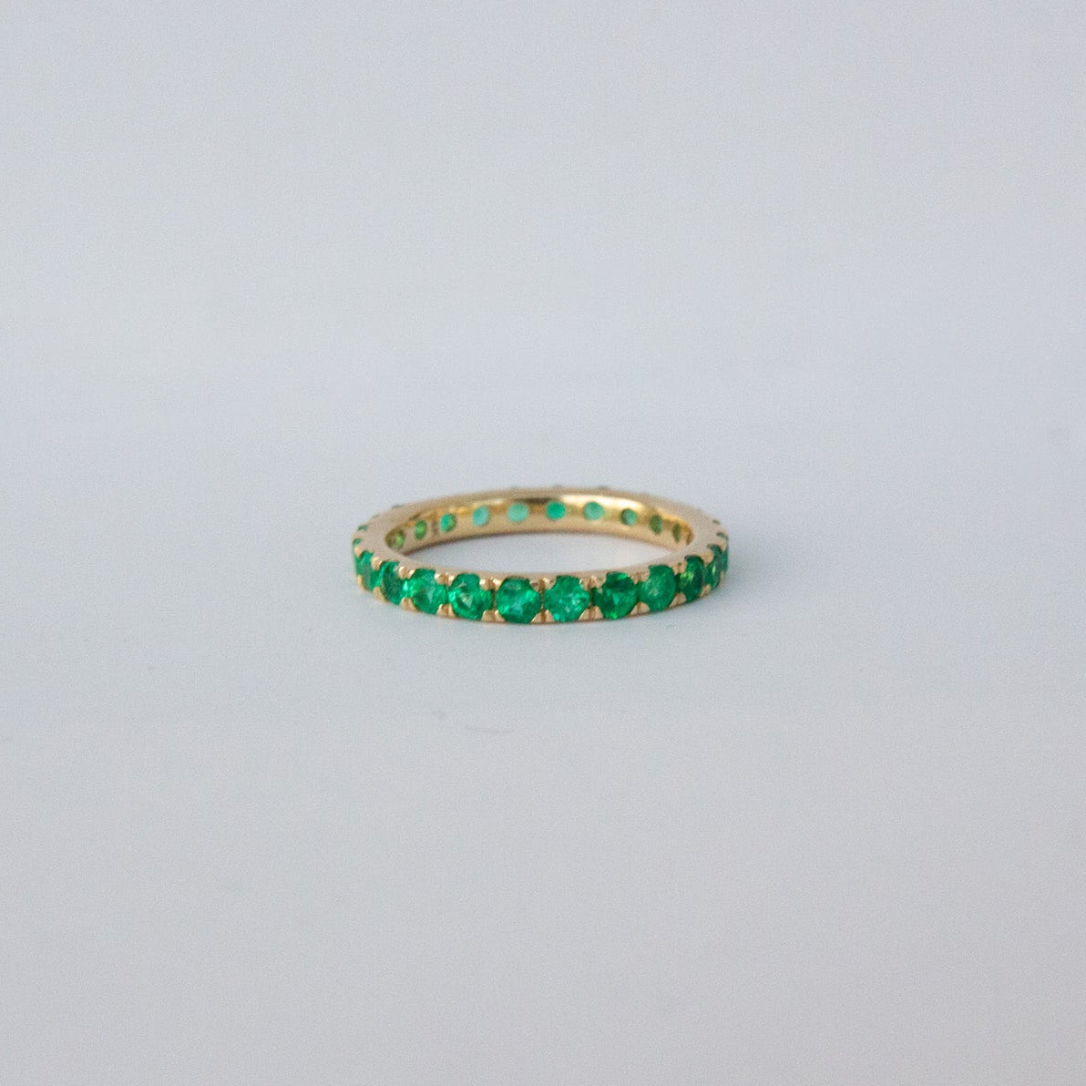 Gold ring with green gemstones on a light gray background