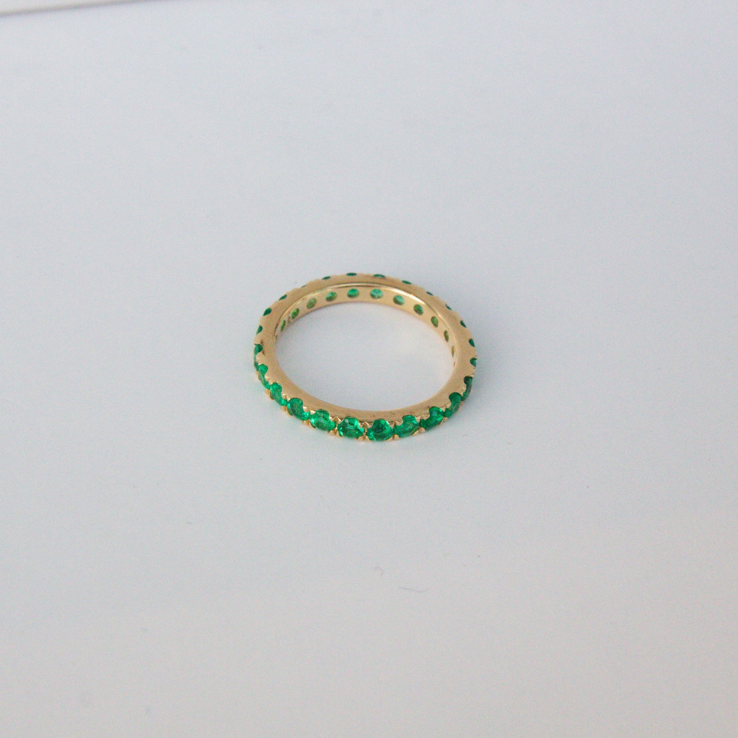 Gold ring with green gemstones on a light gray background