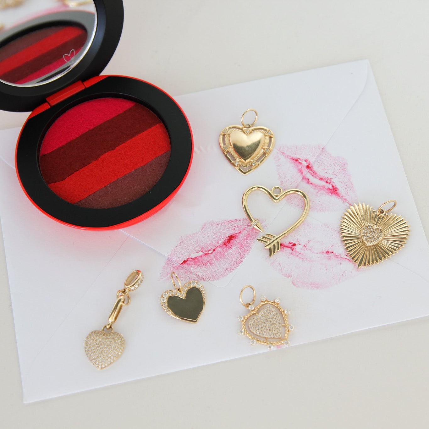 Gold heart-shaped jewelry charms on a white card with a red and black compact mirror.