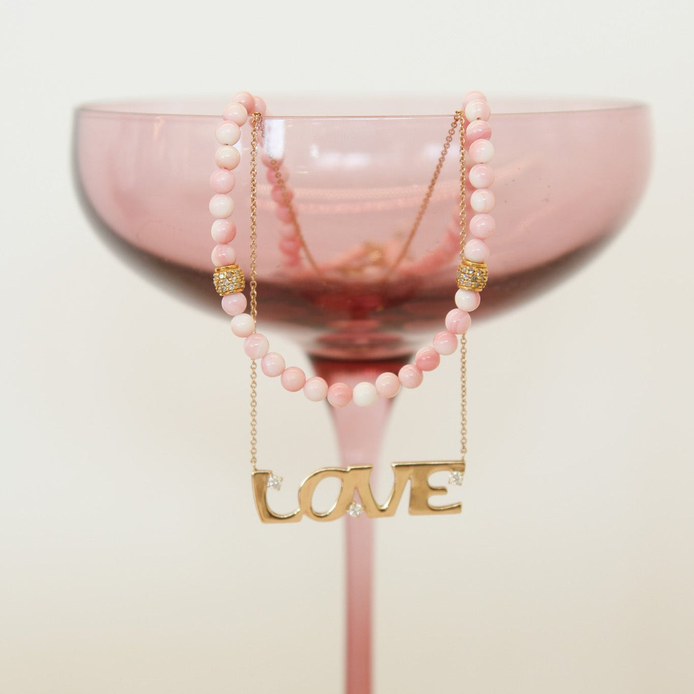 Pink glass with a 'LOVE' necklace on a light background