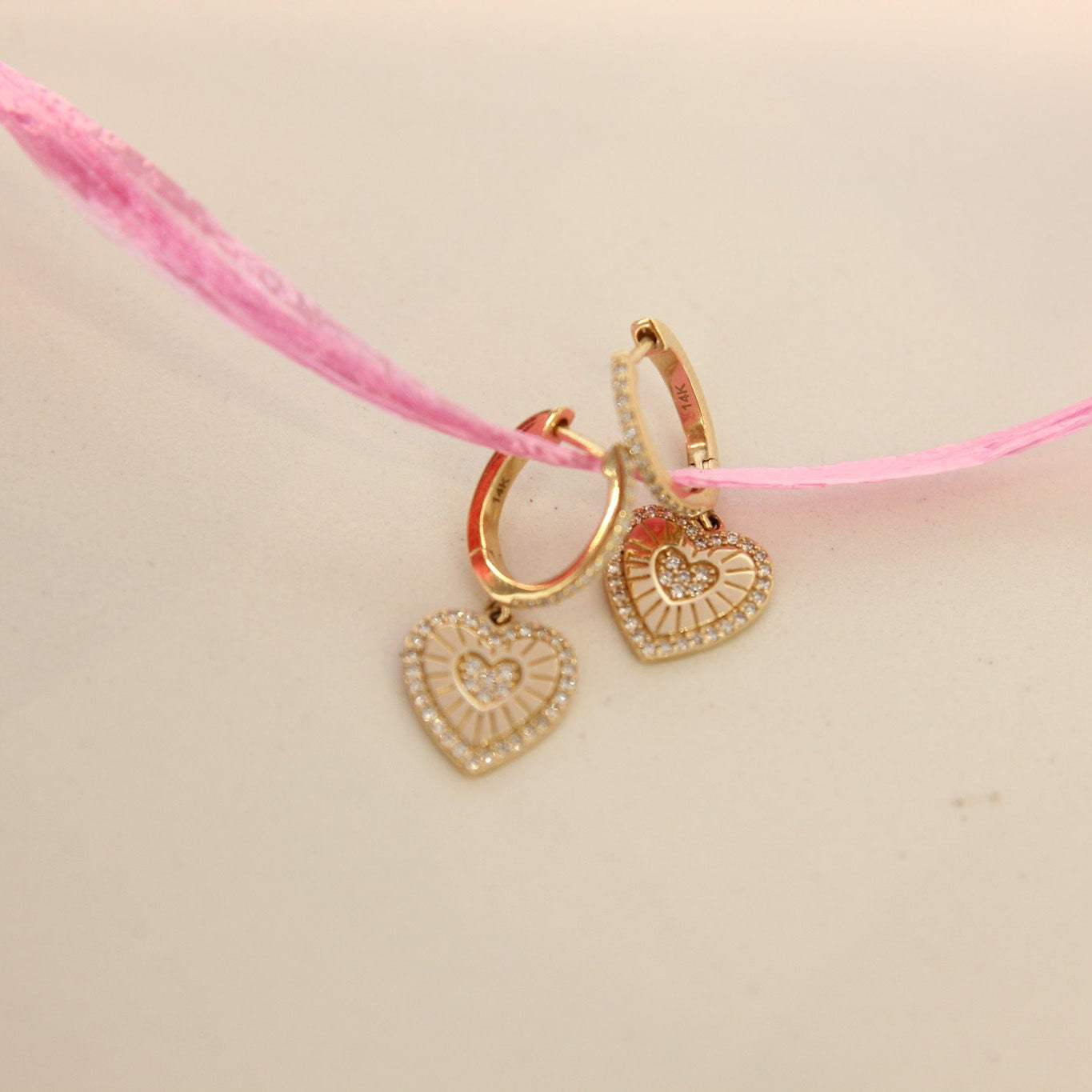 Gold heart-shaped earrings on a pink thread against a beige background
