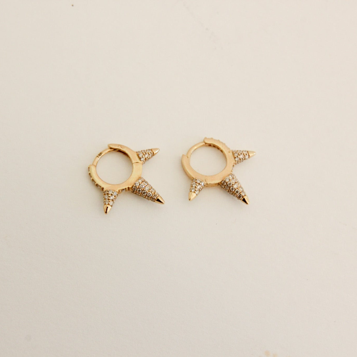 Pair of gold spike earrings on a light beige background