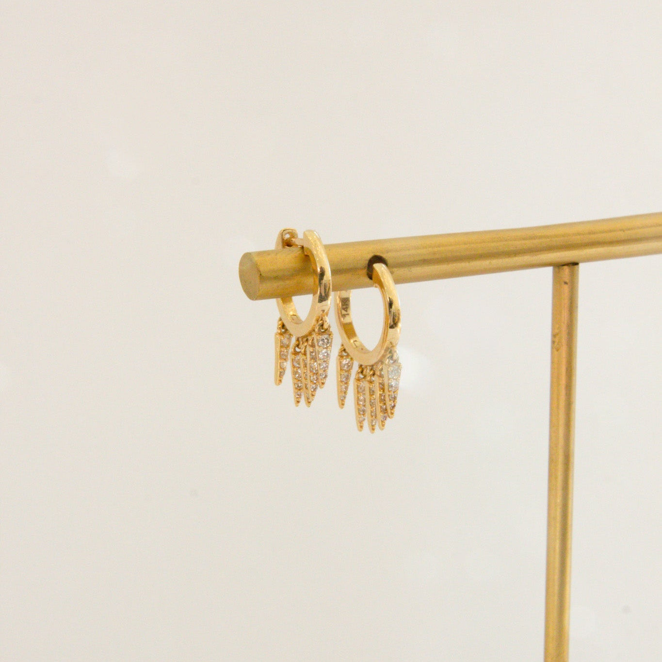 Gold hoop earrings on a gold stand against a beige background