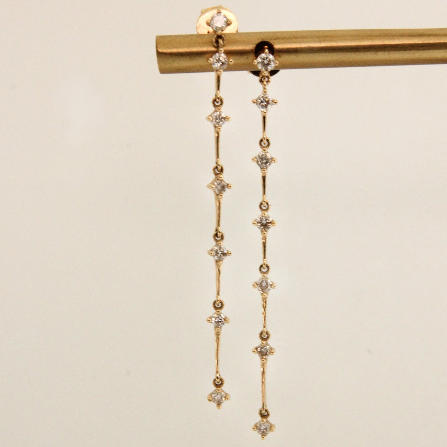 Gold earrings with diamond-like stones on a beige background