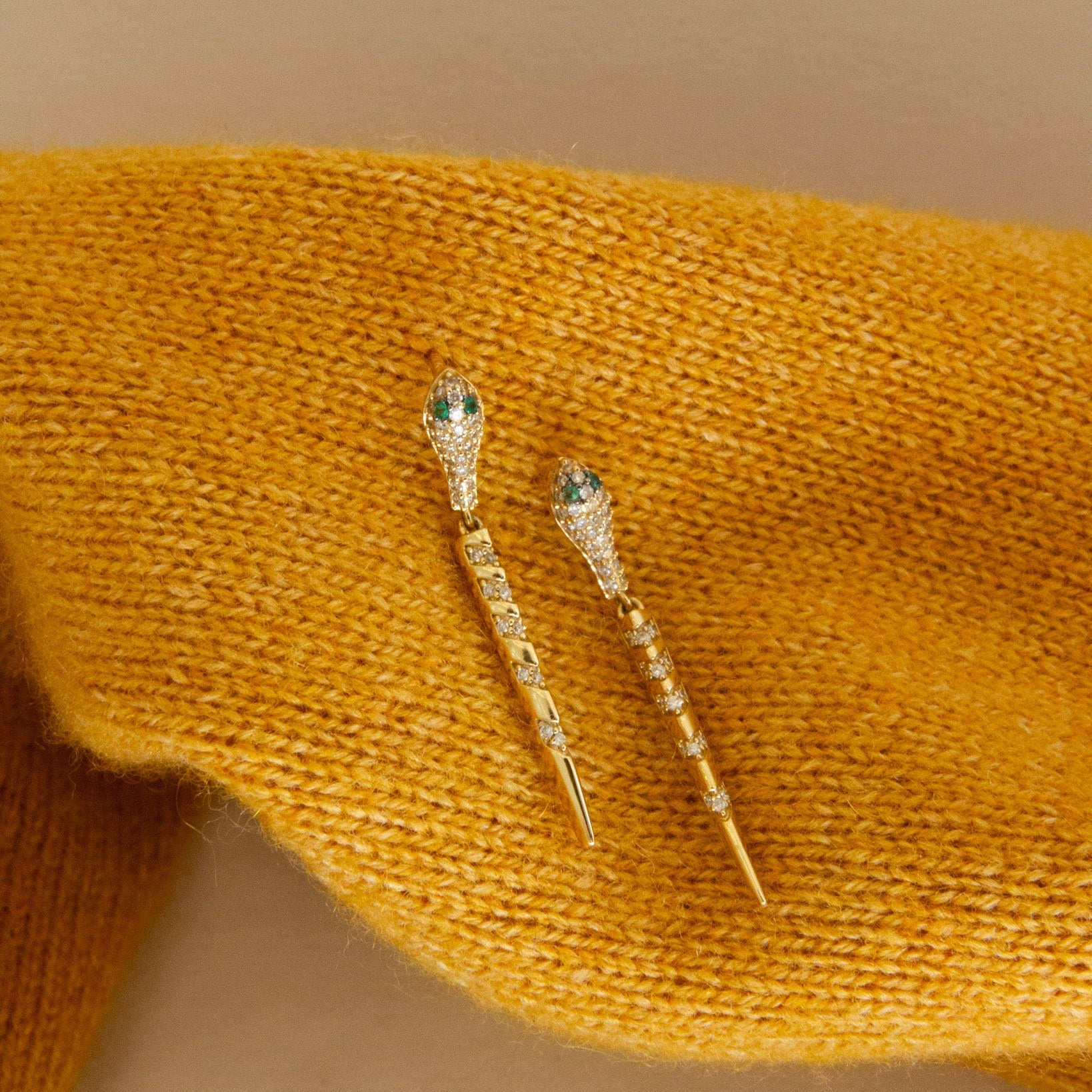 Gold earrings with gemstones on a mustard yellow fabric background