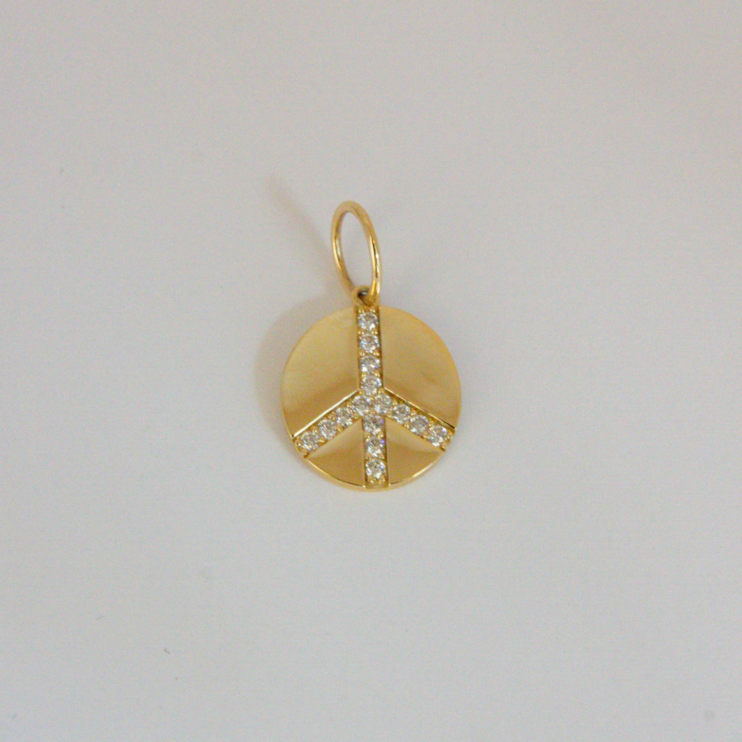 Gold peace sign pendant with clear stones on a light gray background