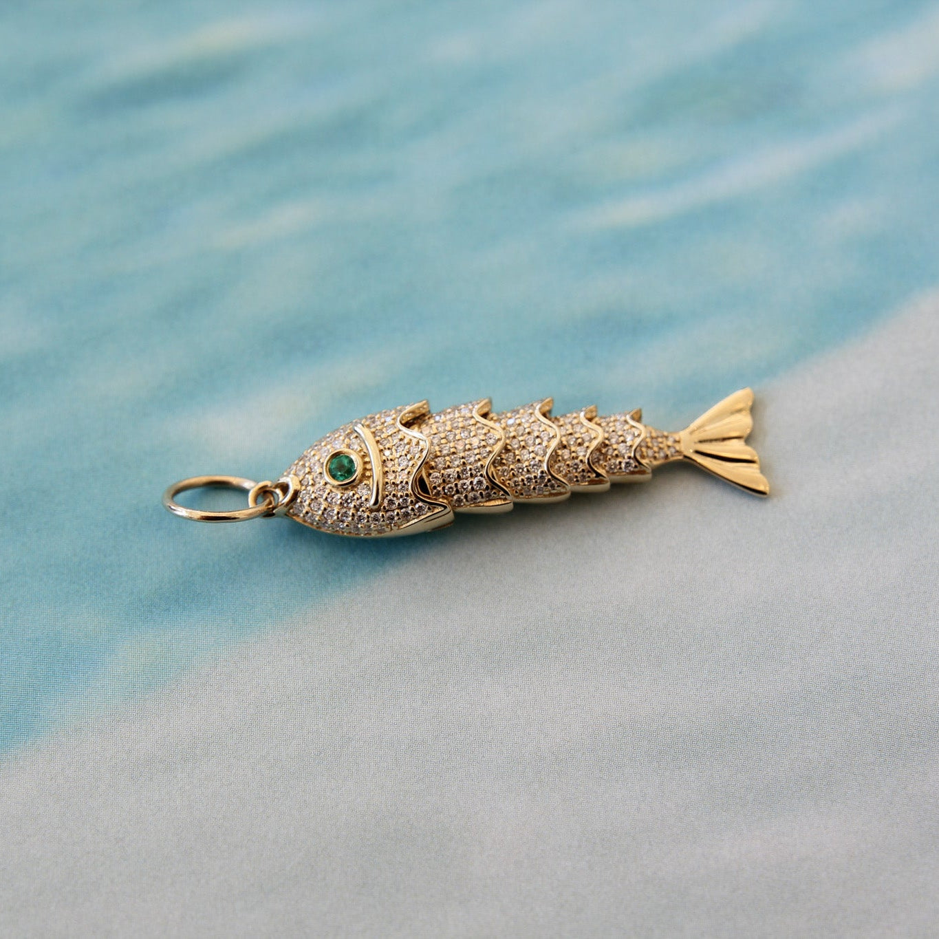 Gold fish-shaped pendant with green stone on a blue and gray gradient background