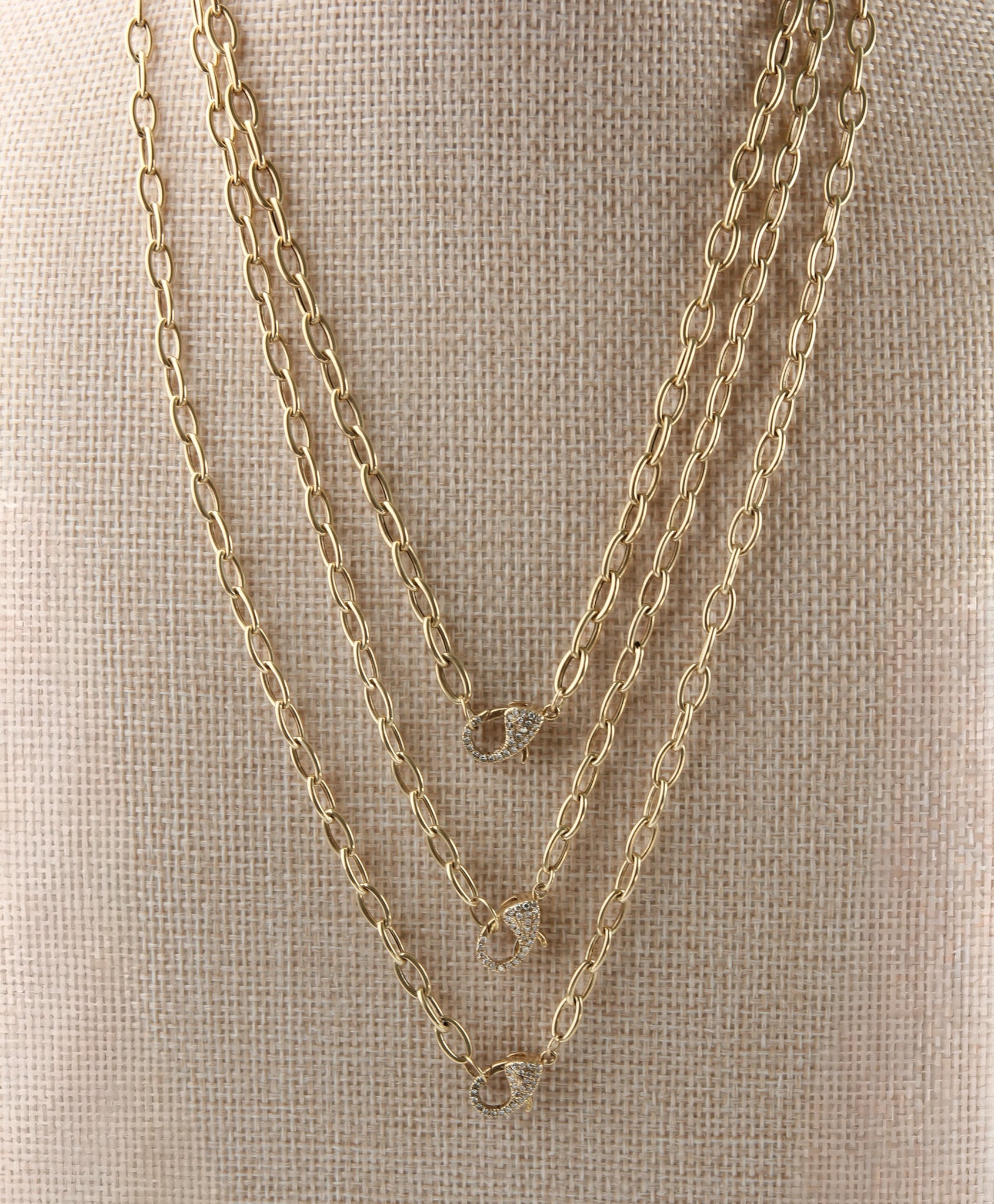 Three gold chain necklaces on a textured beige surface