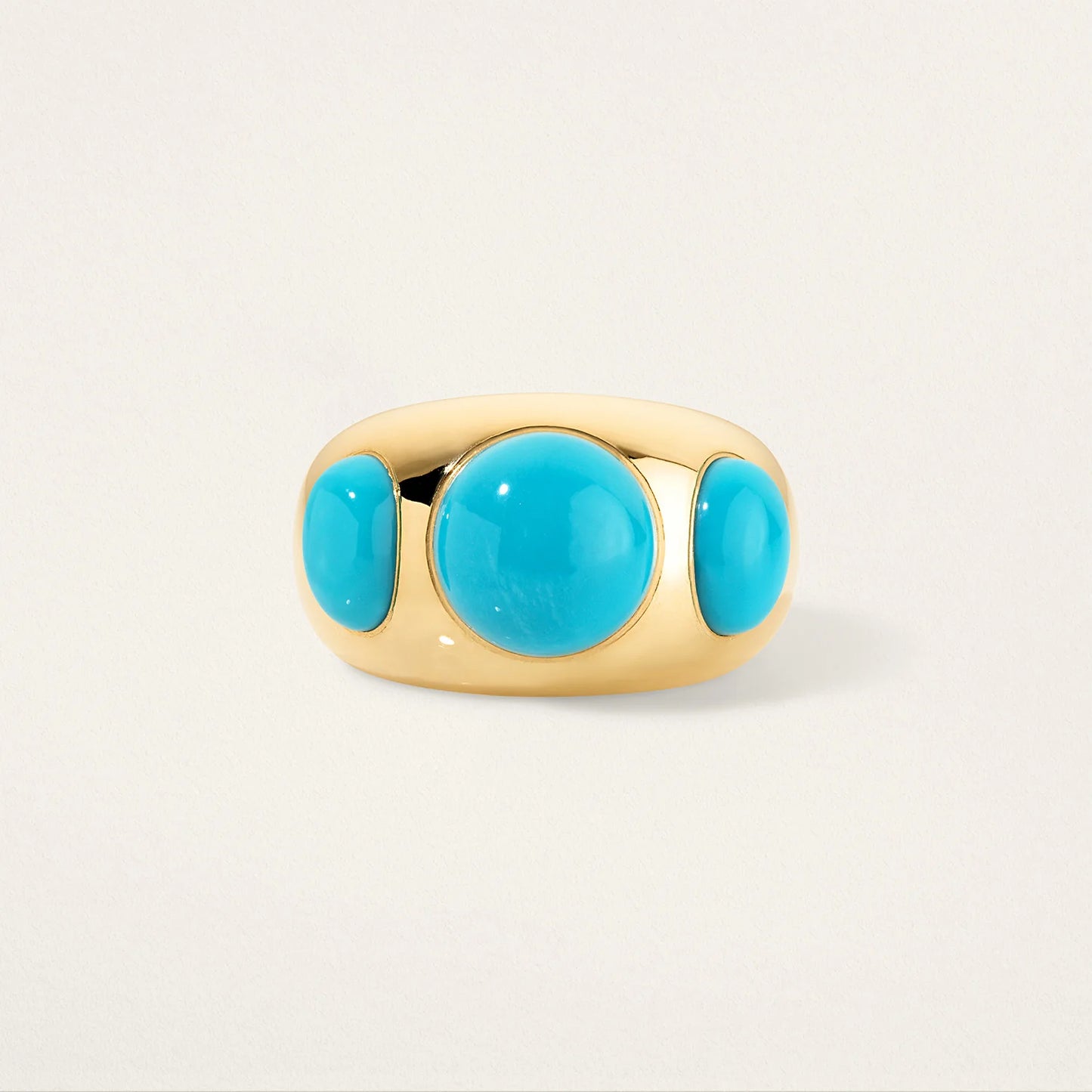 Gold ring with three turquoise stones on a light beige background