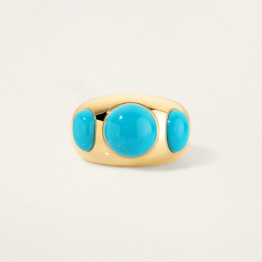 Gold ring with three turquoise stones on a light beige background