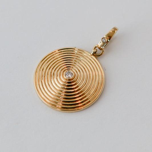 Gold pendant with circular design and diamond on a light gray background