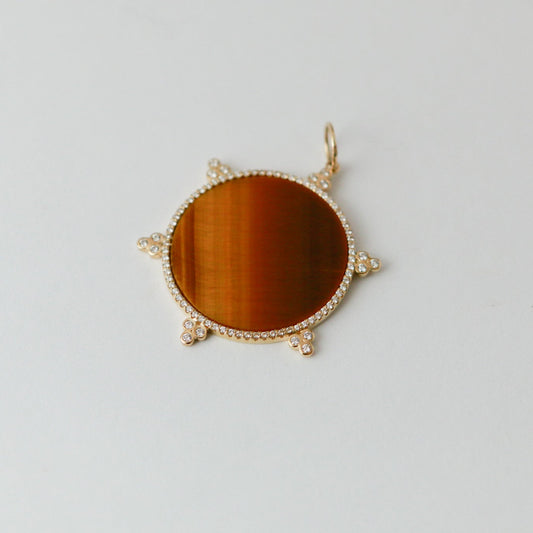 Gold pendant with a round brown stone on a light gray background