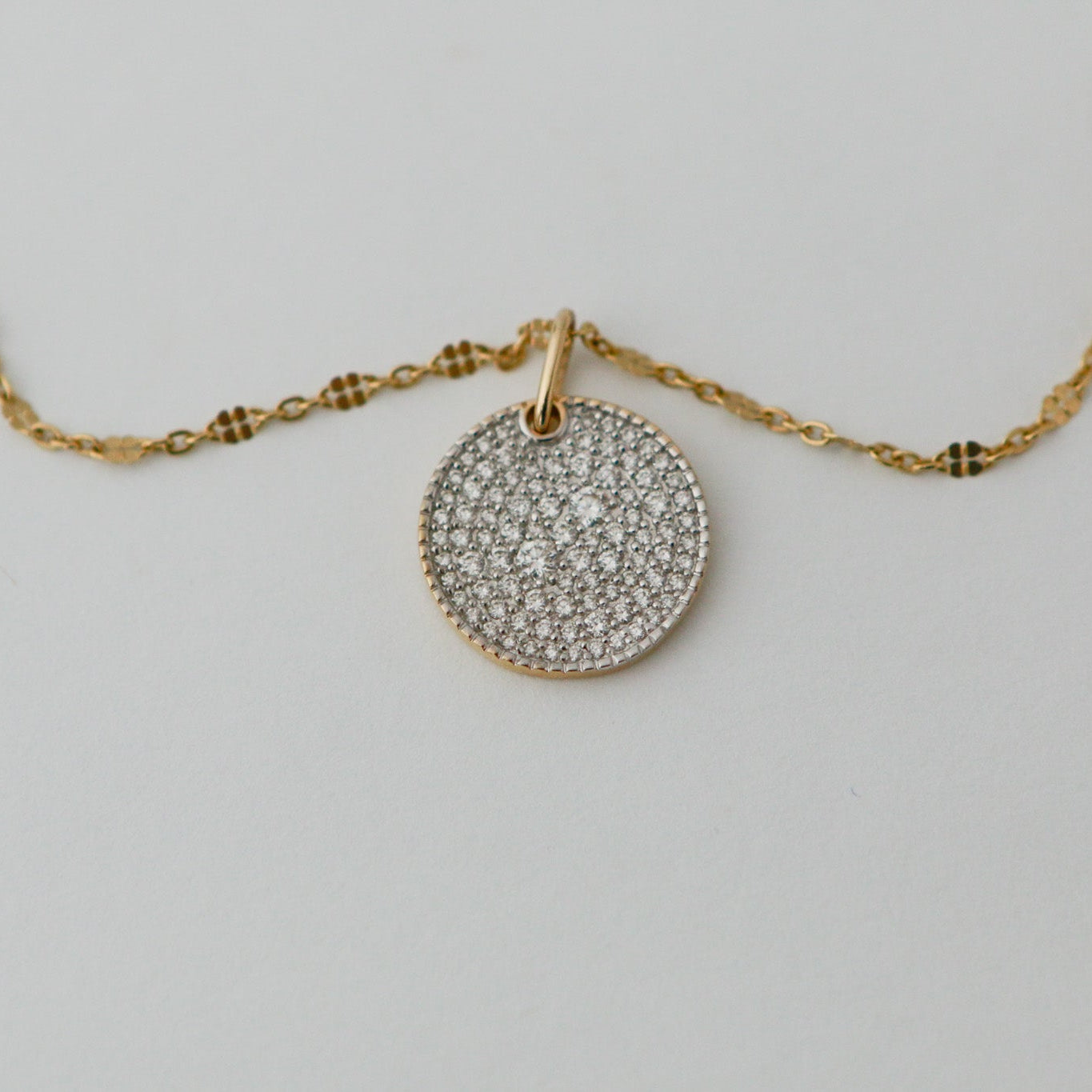 Gold necklace with a round, diamond-studded pendant on a light gray background