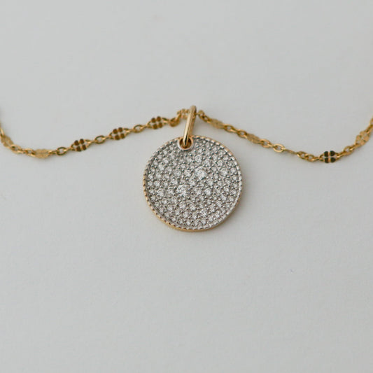 Gold necklace with a round, diamond-studded pendant on a light gray background