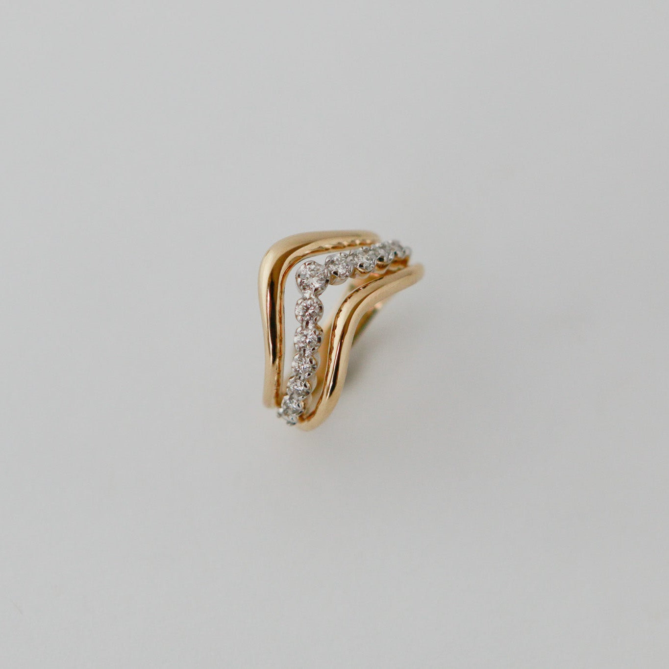 Gold earring with small diamonds on a light gray background