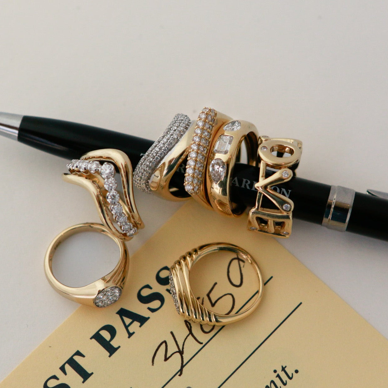 Gold rings with diamond accents on a pen, placed on a document.