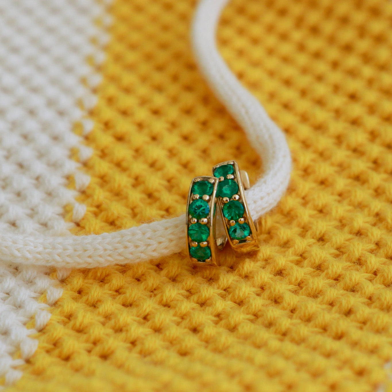 Gold earring with green gemstones on a yellow and white textured fabric background