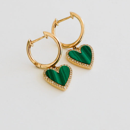 Gold hoop earrings with green heart-shaped charms on a light gray background