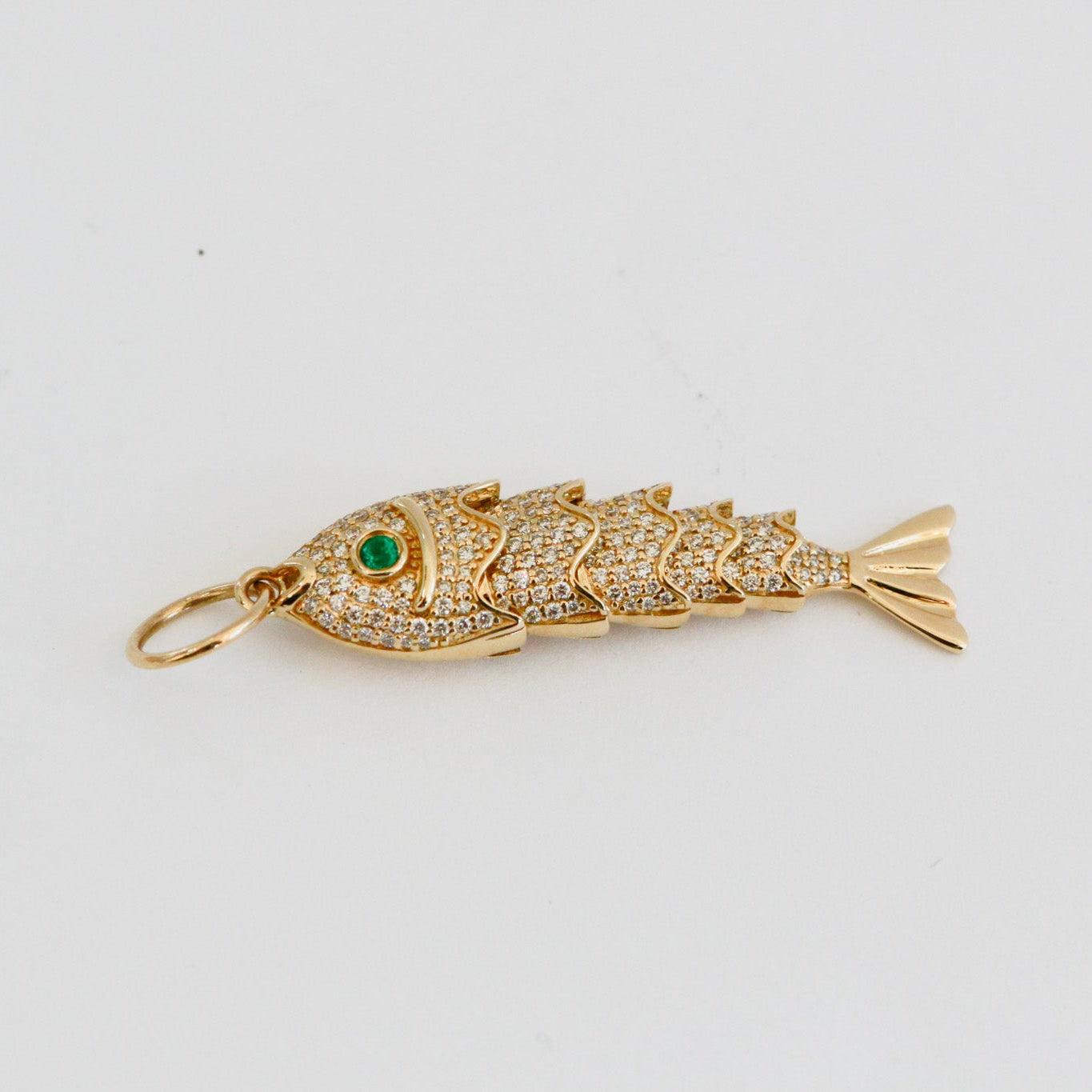 Gold fish-shaped pendant with emerald eye on a light gray background