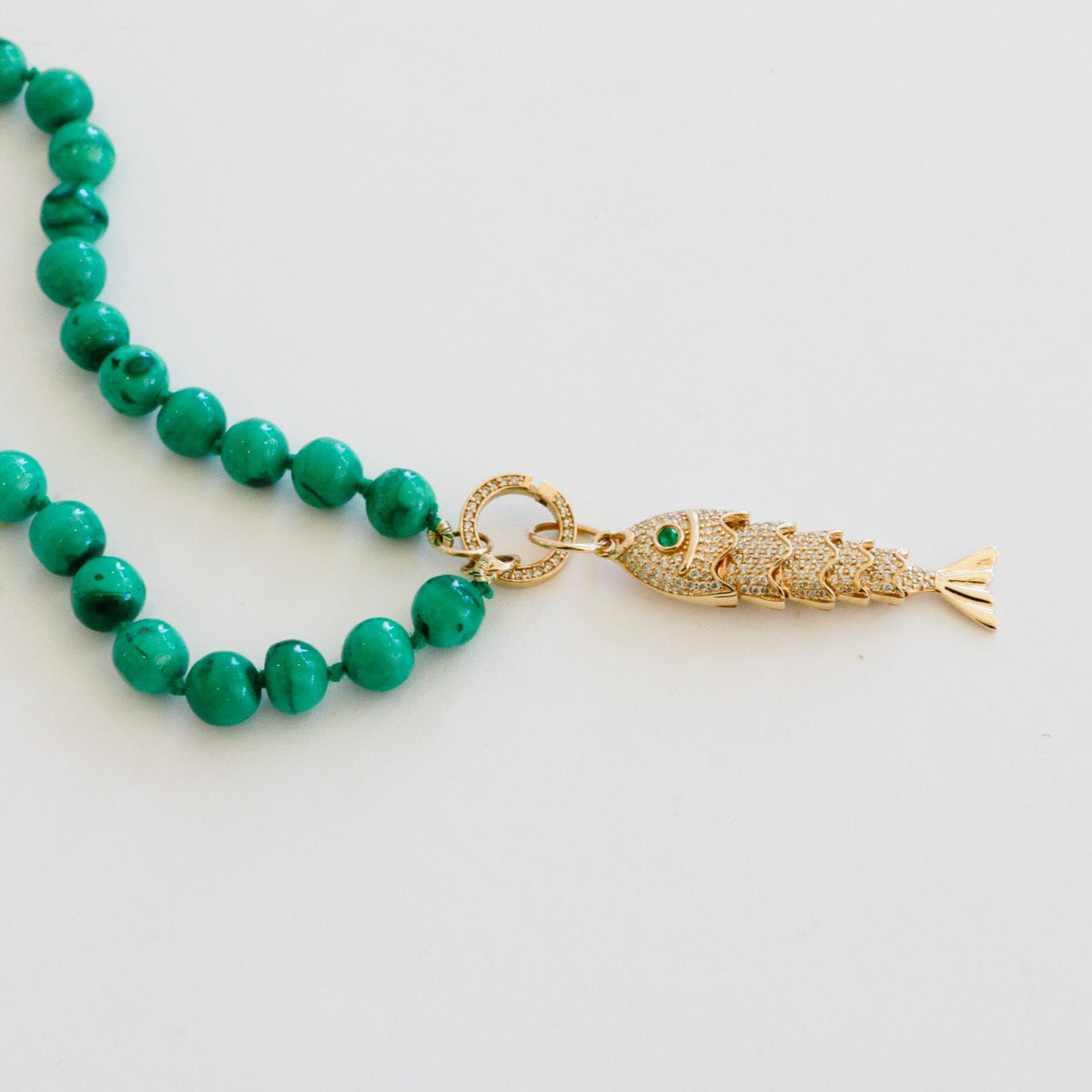 Green beaded necklace with a gold fish pendant on a white background