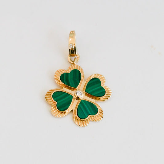 Gold four-leaf clover pendant with green enamel on a light gray background