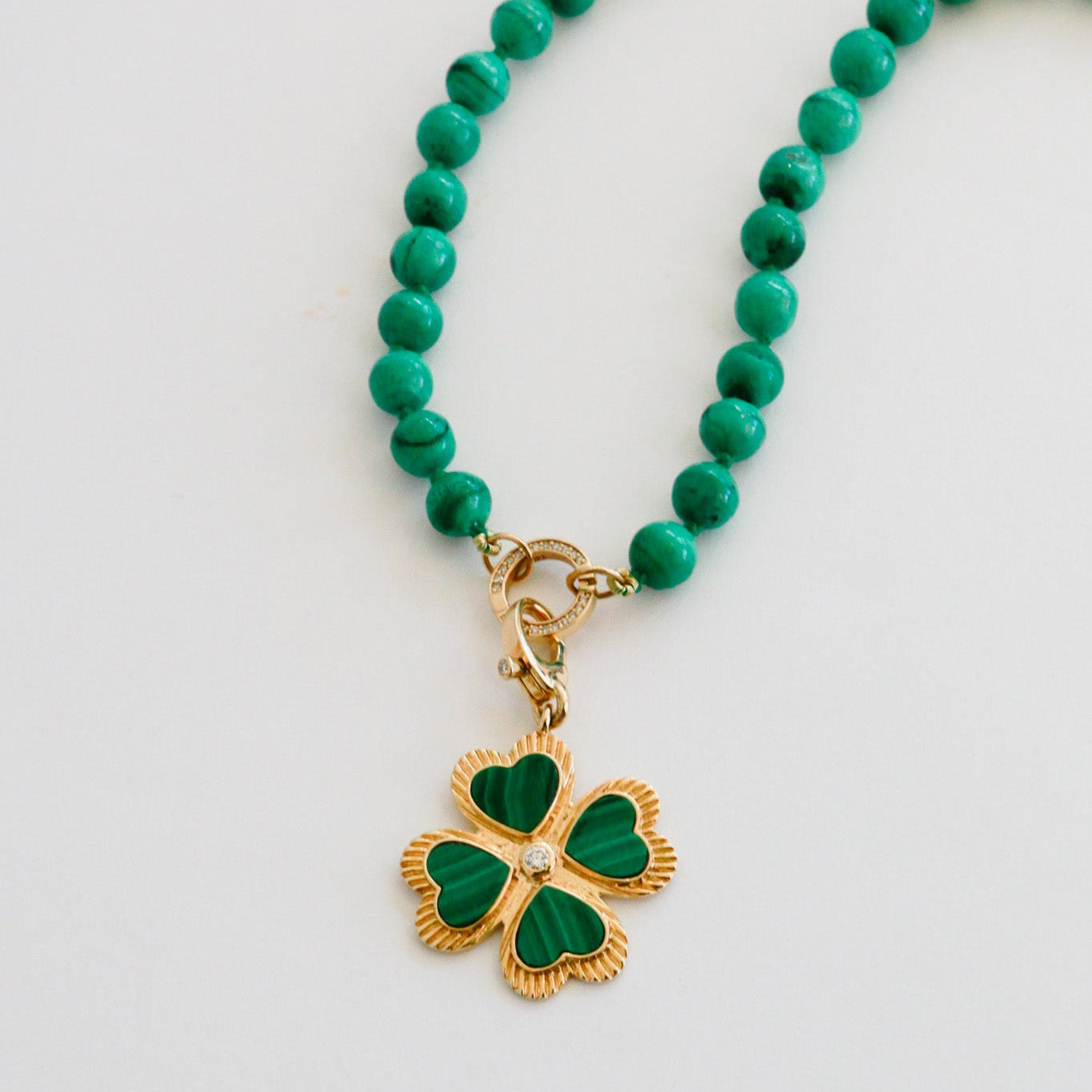 Necklace with green beads and a gold four-leaf clover charm on a light gray background