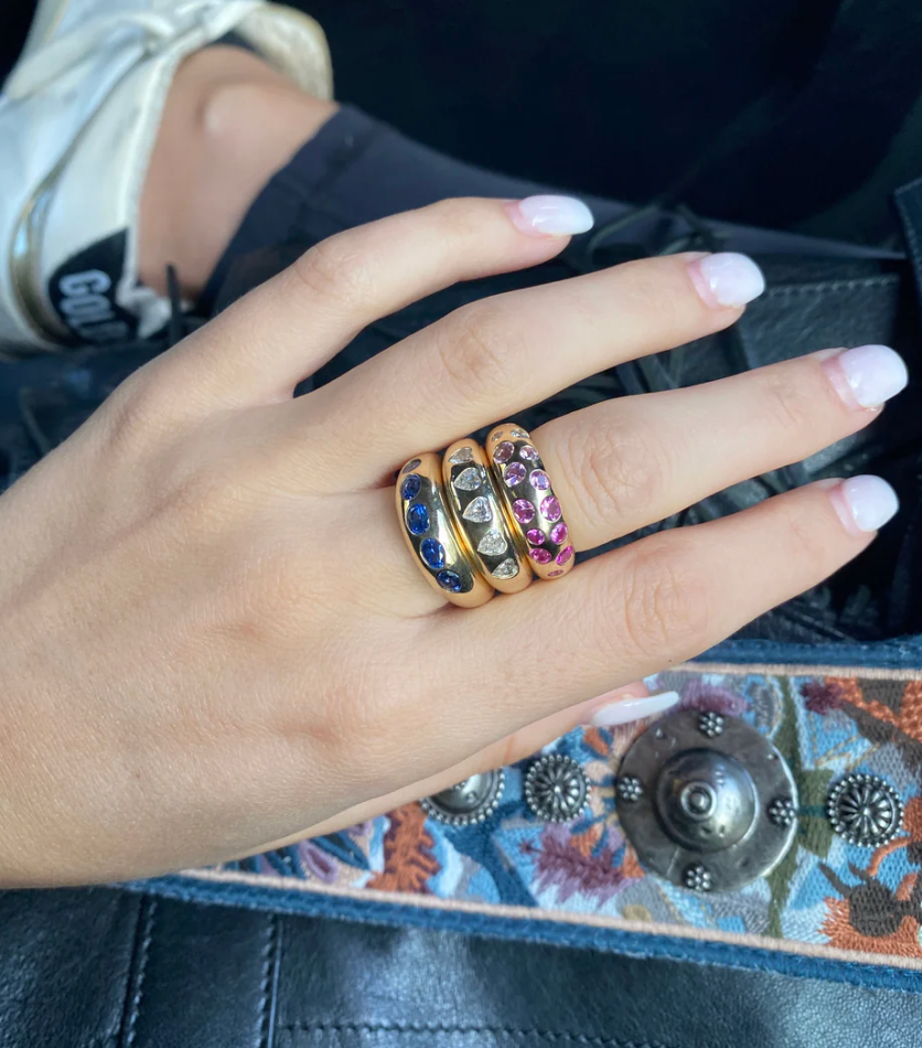 Hand wearing three rings with gemstones on a textured surface