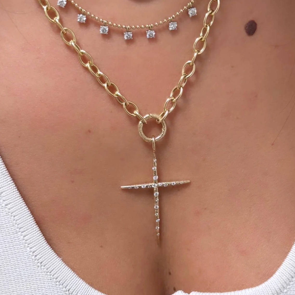 Gold chain necklace with a diamond cross pendant on a person wearing a white top.