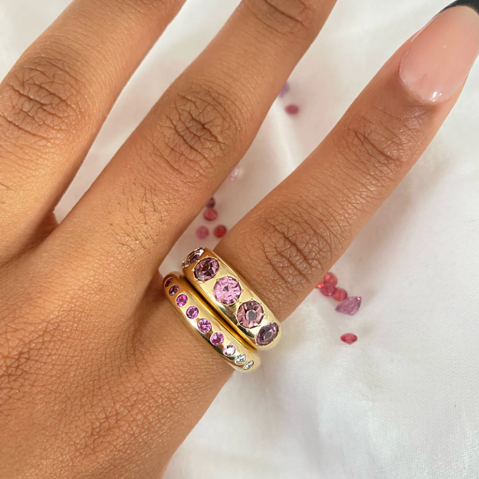 Gold ring with pink gemstones on a hand against a white background